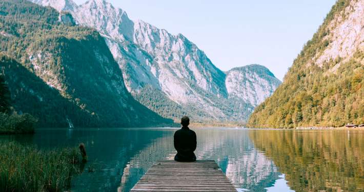 person meditating in a meditation posture in front of a contemplative lake
