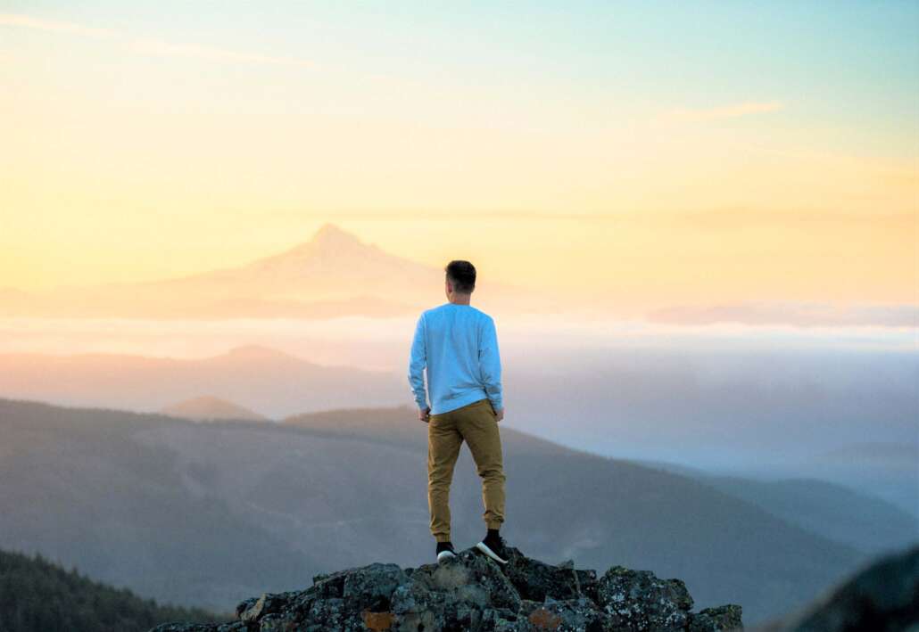 man standing on mountain looking at sunset